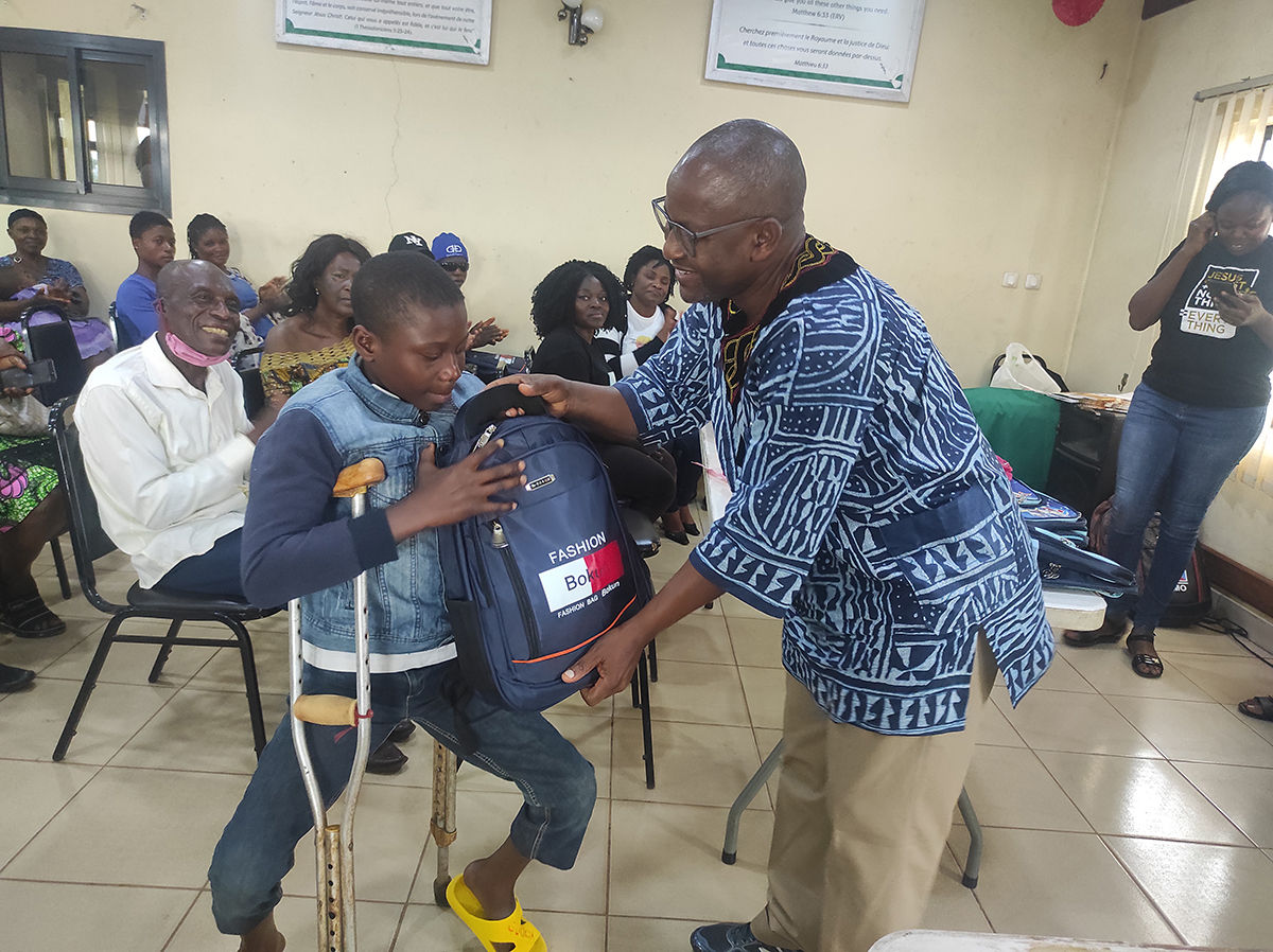 CBR supervisor handing school bag to a child with disability
