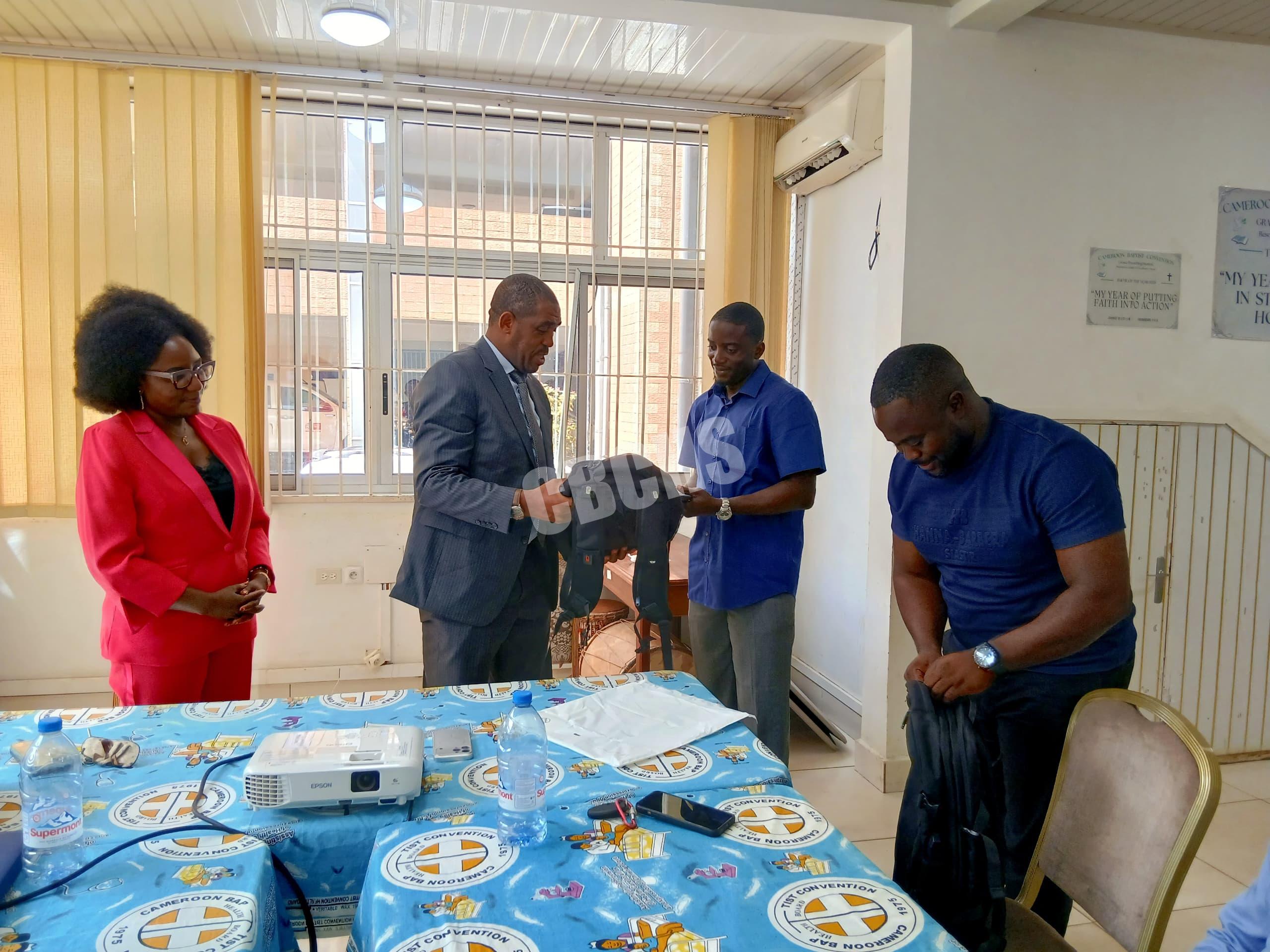 The Director of CBCHS Mr Ngum Samuel hands over laptops and laptop bags to trainees