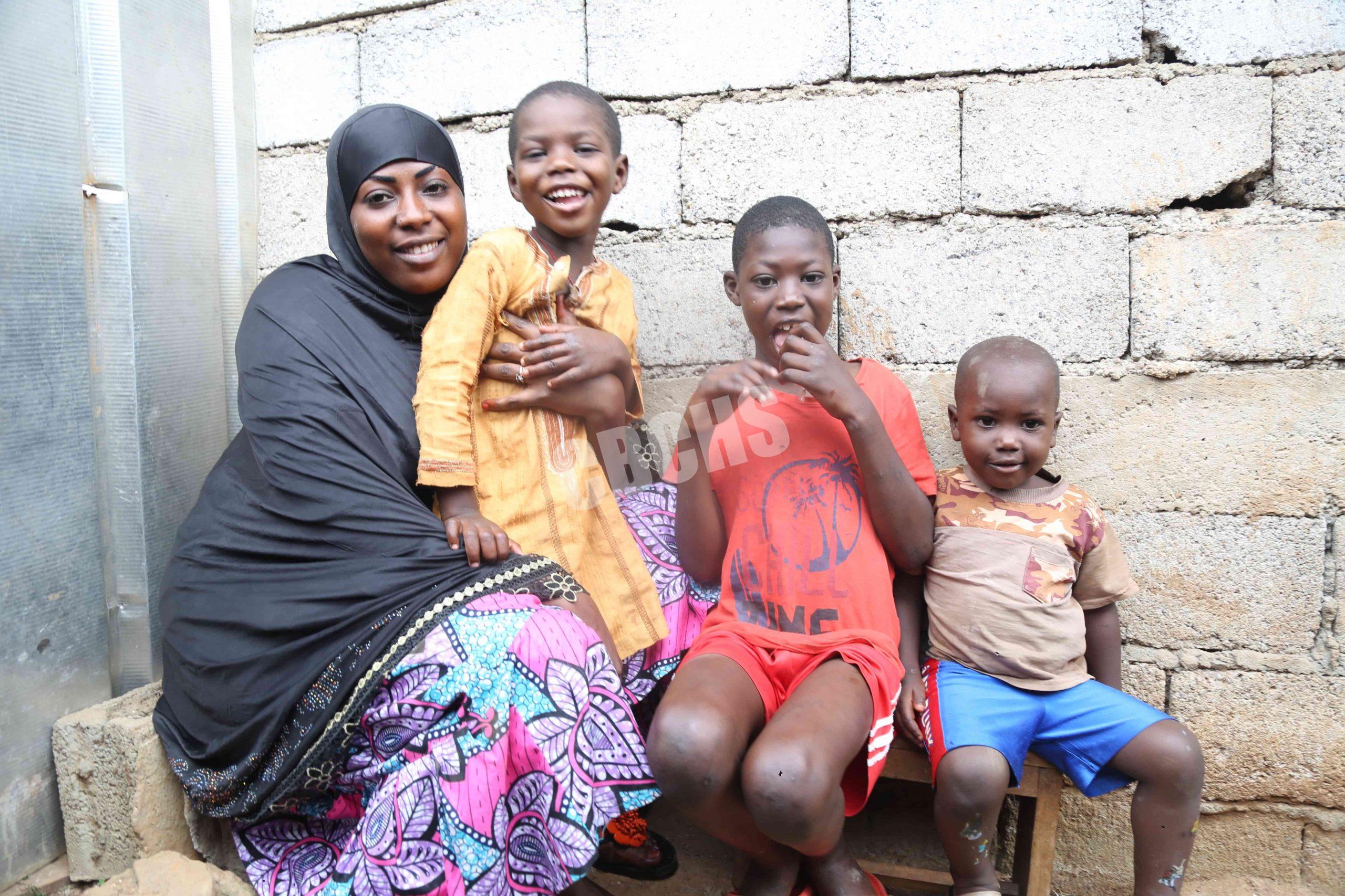 herif in red, Yakoubou in yellow, their mother, and younger brother share a bright, joyful moment outdoors—radiating family love and happiness.